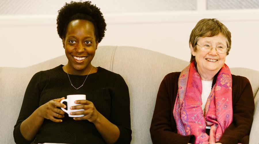 A millennial and a Catholic sister sit together, smiling.