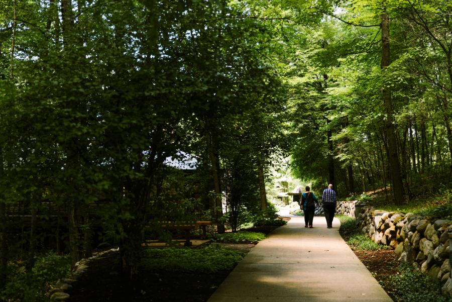 Mary Ann and Frederic Brussat walk down a wooded path to Seasons Retreat Center