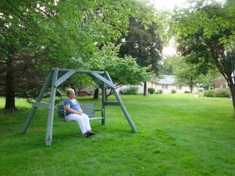 woman sits alone on a bench swing in a green grassy yard