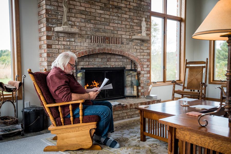 man sitting in glider chair in front of brick fireplace