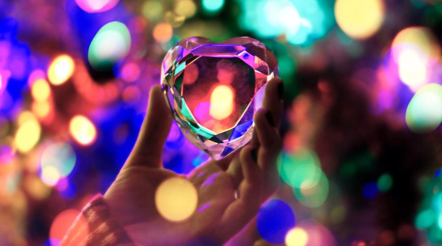 Hand holding multi-faceted glass heart amidst colored lights