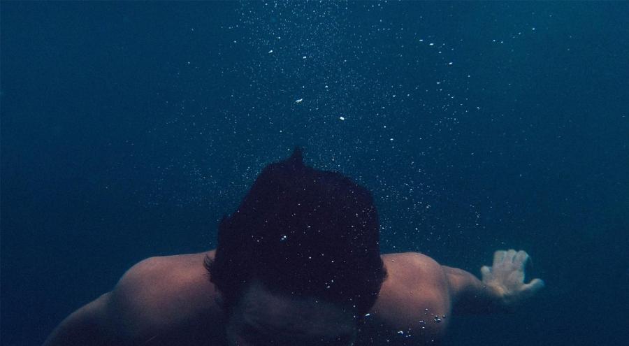 Man swimming underwater evocative of diving under emotions