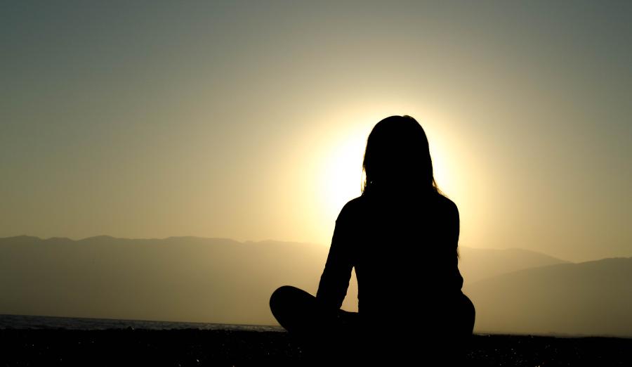 Silhouette of person seated cross-legged taking pause to watch sunset