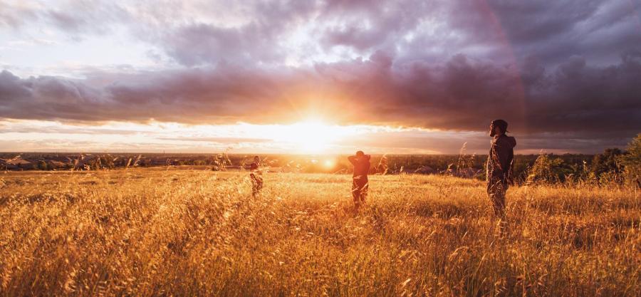 Sunburst on field with three people silhouetted