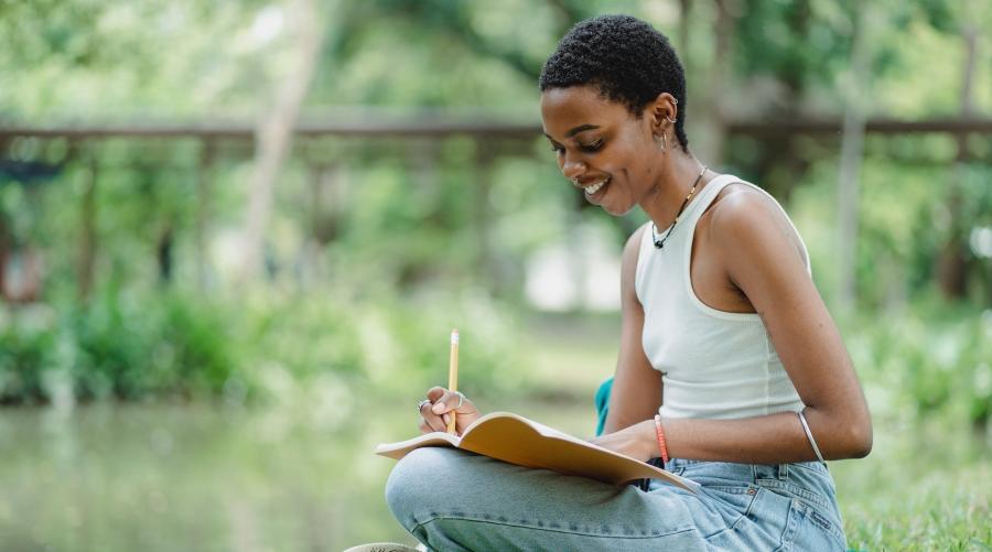 Black woman sitting cross-legged drawing outdoors