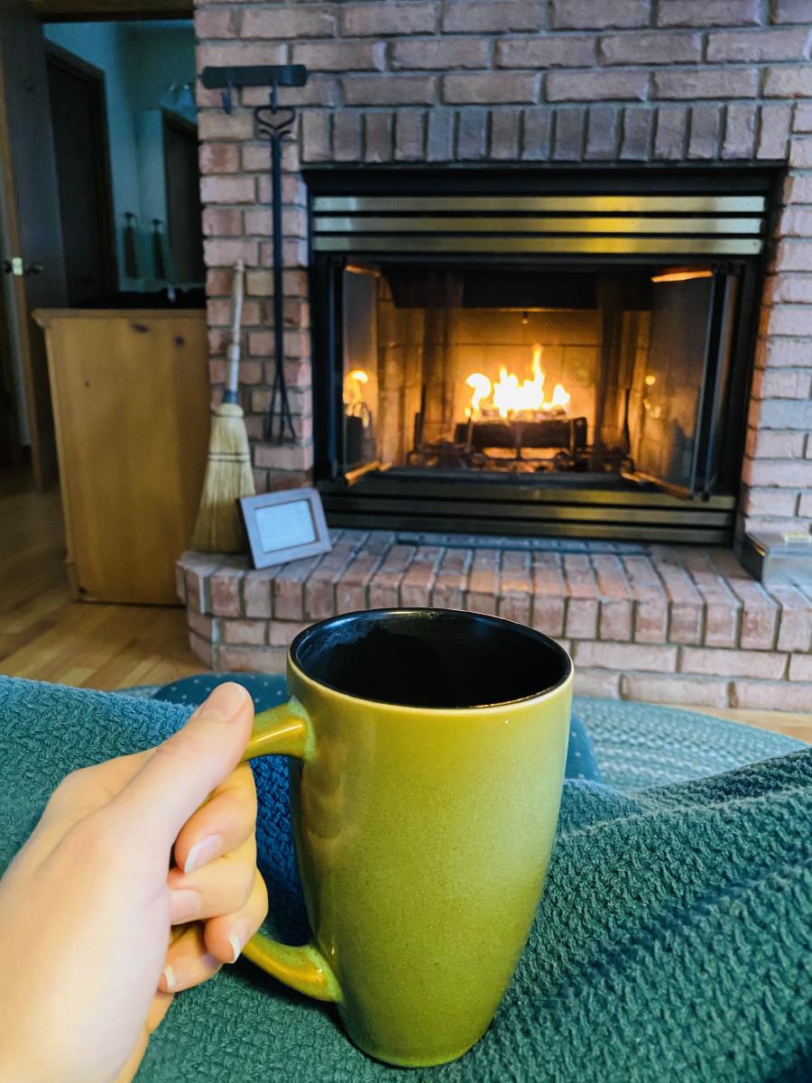 green coffee cup in hand in front of fireplace