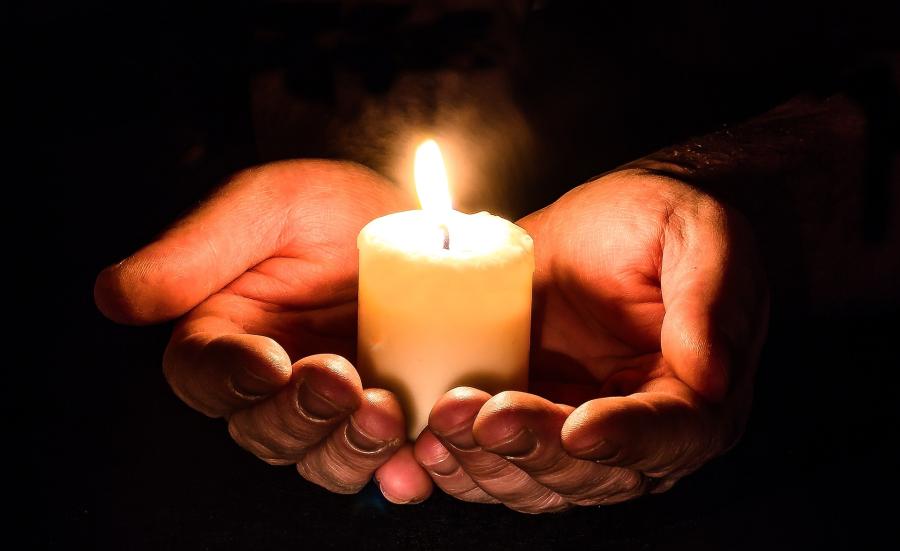 hands holding lit candle in front of dark background